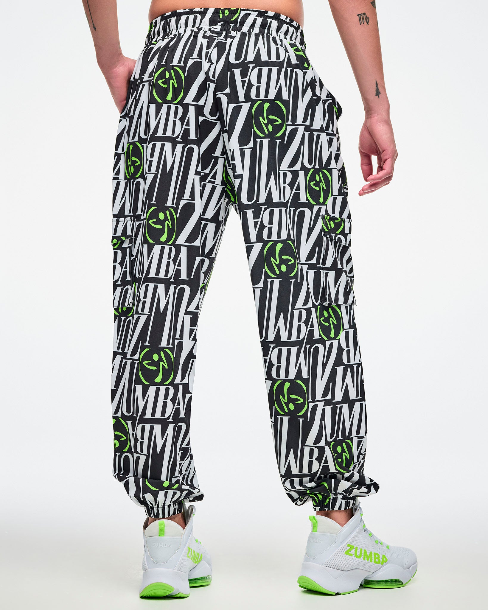 Back view of a male model wearing black and white patterned pants with green Zumbito accents on a white background.