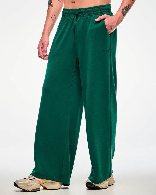 Male model in the teal green high-waisted pants, turned slightly to show the wide, relaxed leg, paired with beige platform shoes.