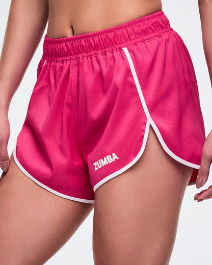 Pink Zumba shorts with white trim and small white Zumba text on the left leg worn by a female model.