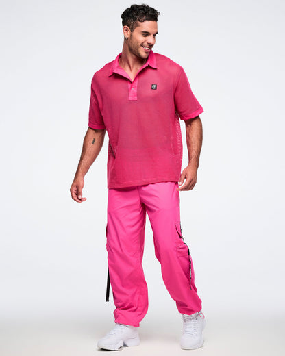 Male model wearing a pink mesh polo with matching pink cargo pants and white shoes.