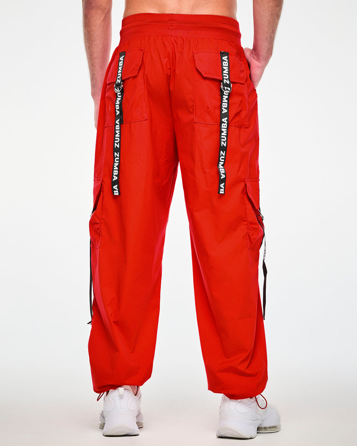 Back view of a male model in the red cargo pants, showing two back cargo pockets, each with a black 'ZUMBA' webbing strap hanging from a silver D-ring.