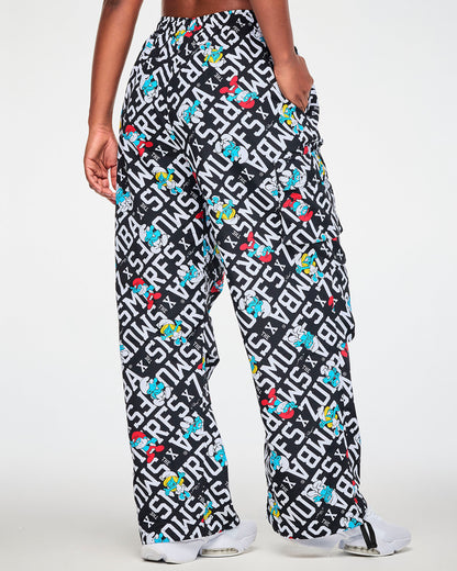 Shown from the back, a female model in the black and white Smurfs print cargo pants, with the print continuing across the seat, a cargo pocket on the side of the leg, and a drawcord hanging at the hem.