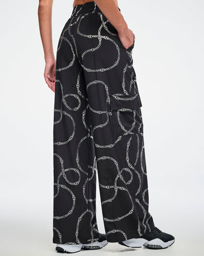 Back view of the black cargo pants with silver chain pattern worn by a female model and paired with black and white shoes.
