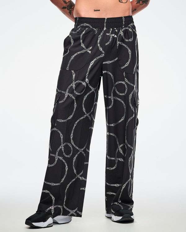Front view of a male model wearing black cargo pants with silver chain pattern, paired with black and white shoes.
