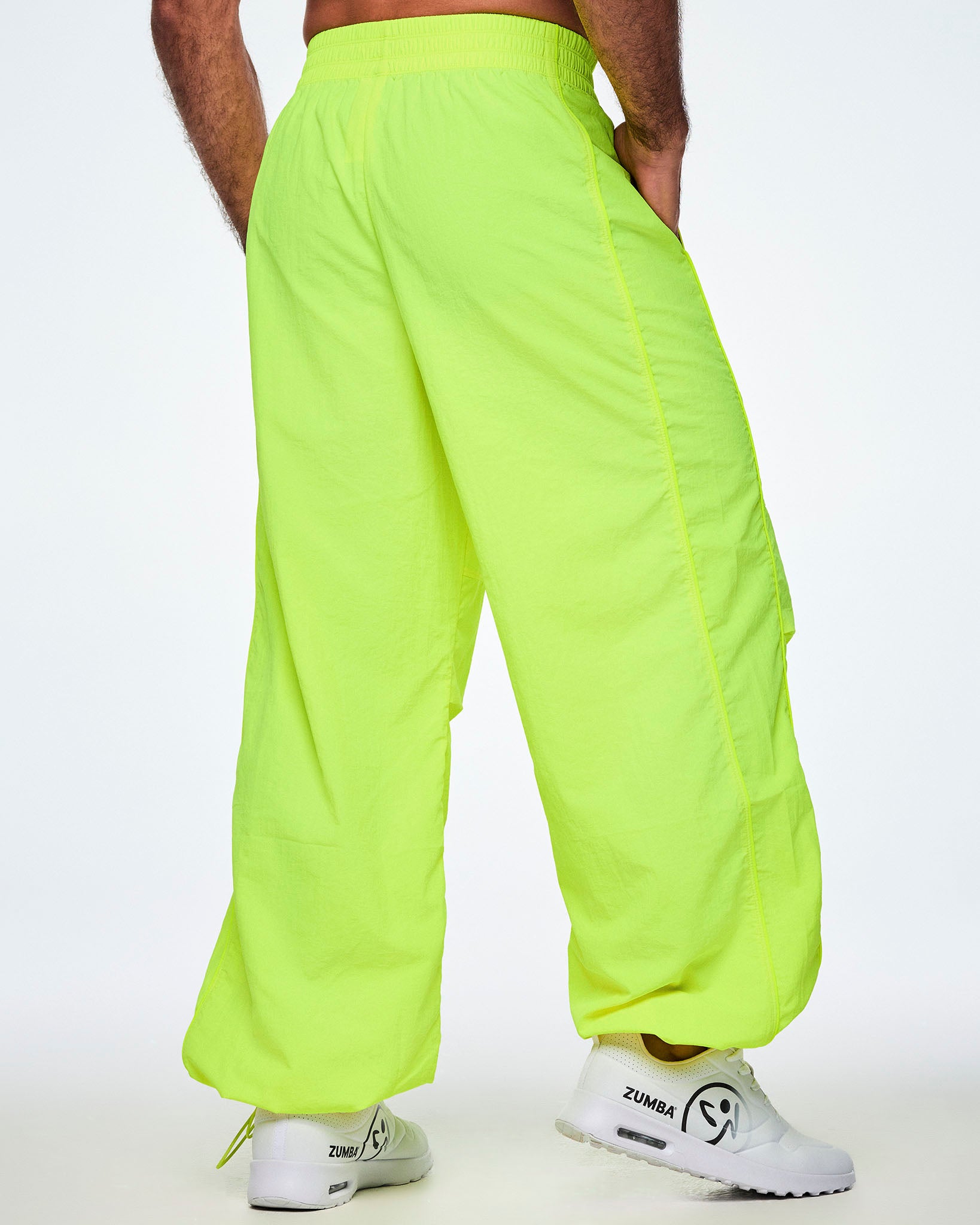 Back view of a male model wearing bright yellow-green Zumba pants with white shoes.