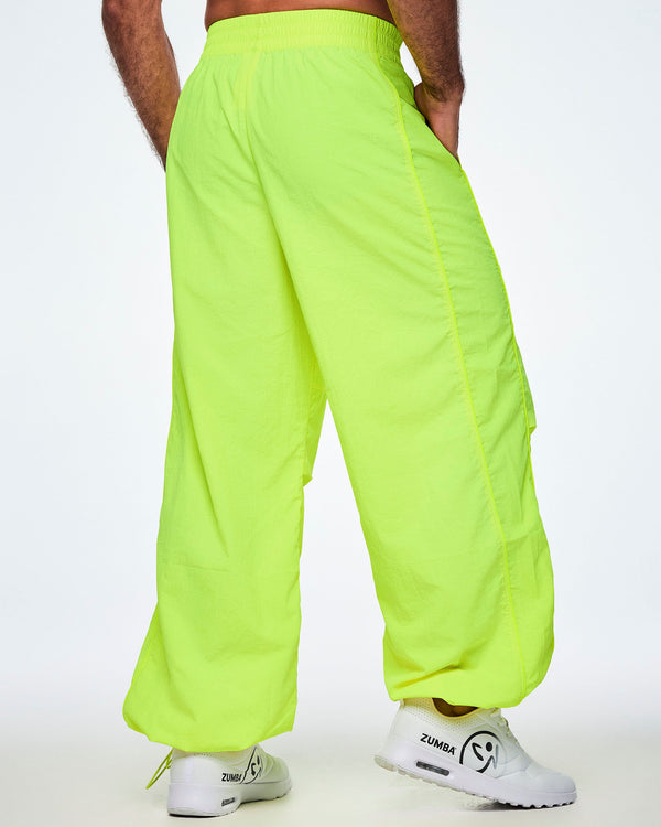 Back view of a male model wearing bright yellow-green Zumba pants with white shoes.