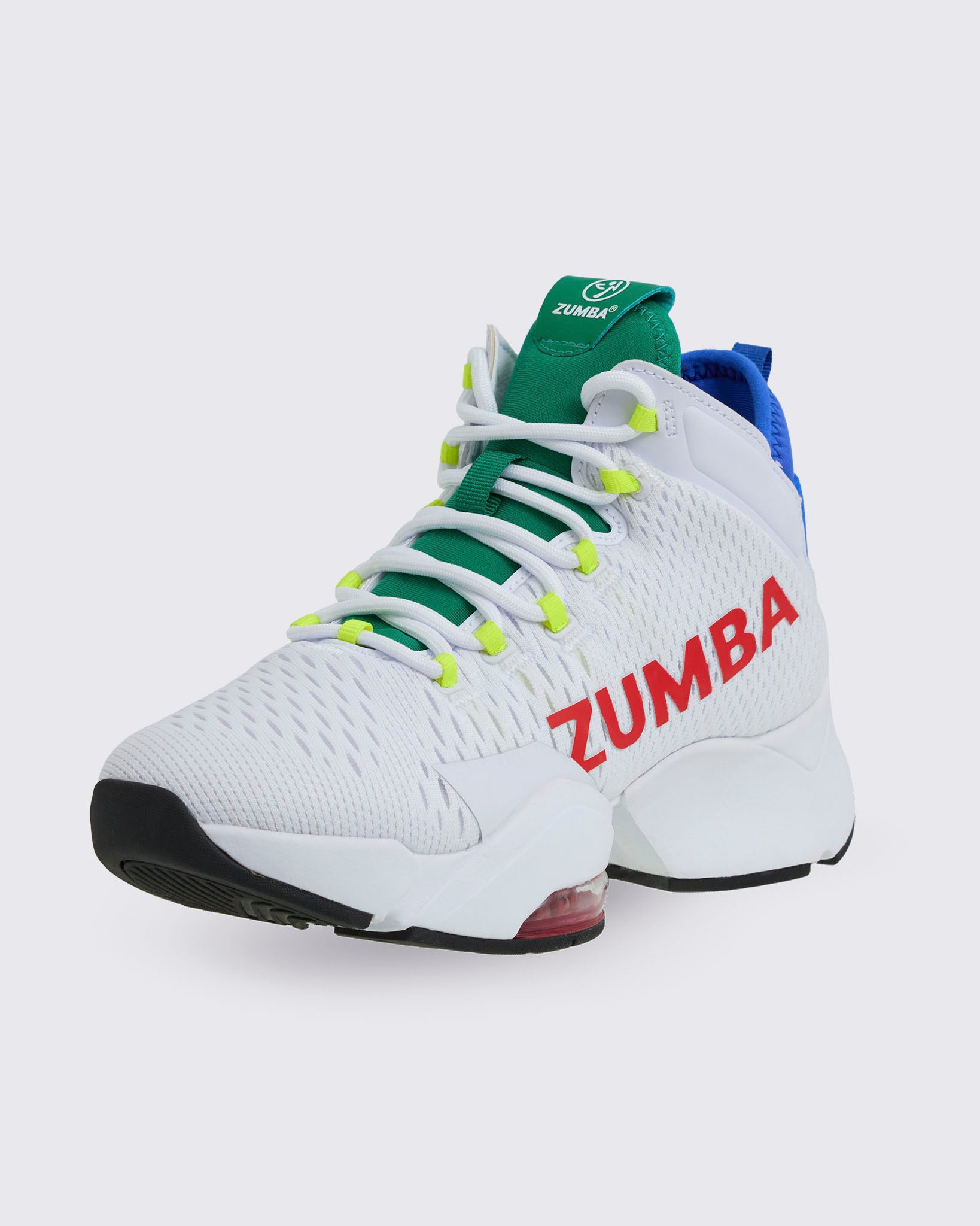 White Zumba high-top dance sneaker with red “ZUMBA” side logo, green tongue, white laces with neon yellow eyelets, blue heel collar, and chunky white sole with red air unit, shown on a light gray background.