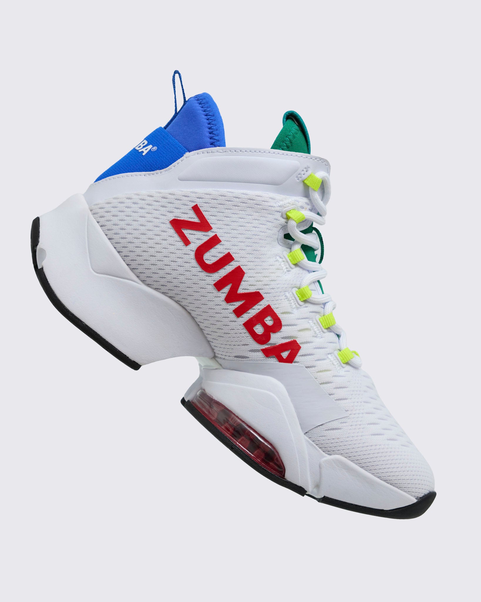 Side view of white Zumba high-top dance sneaker with red “ZUMBA” logo, green tongue, neon yellow lace loops, blue heel collar, and thick white midsole with red air unit, photographed on a light gray background.