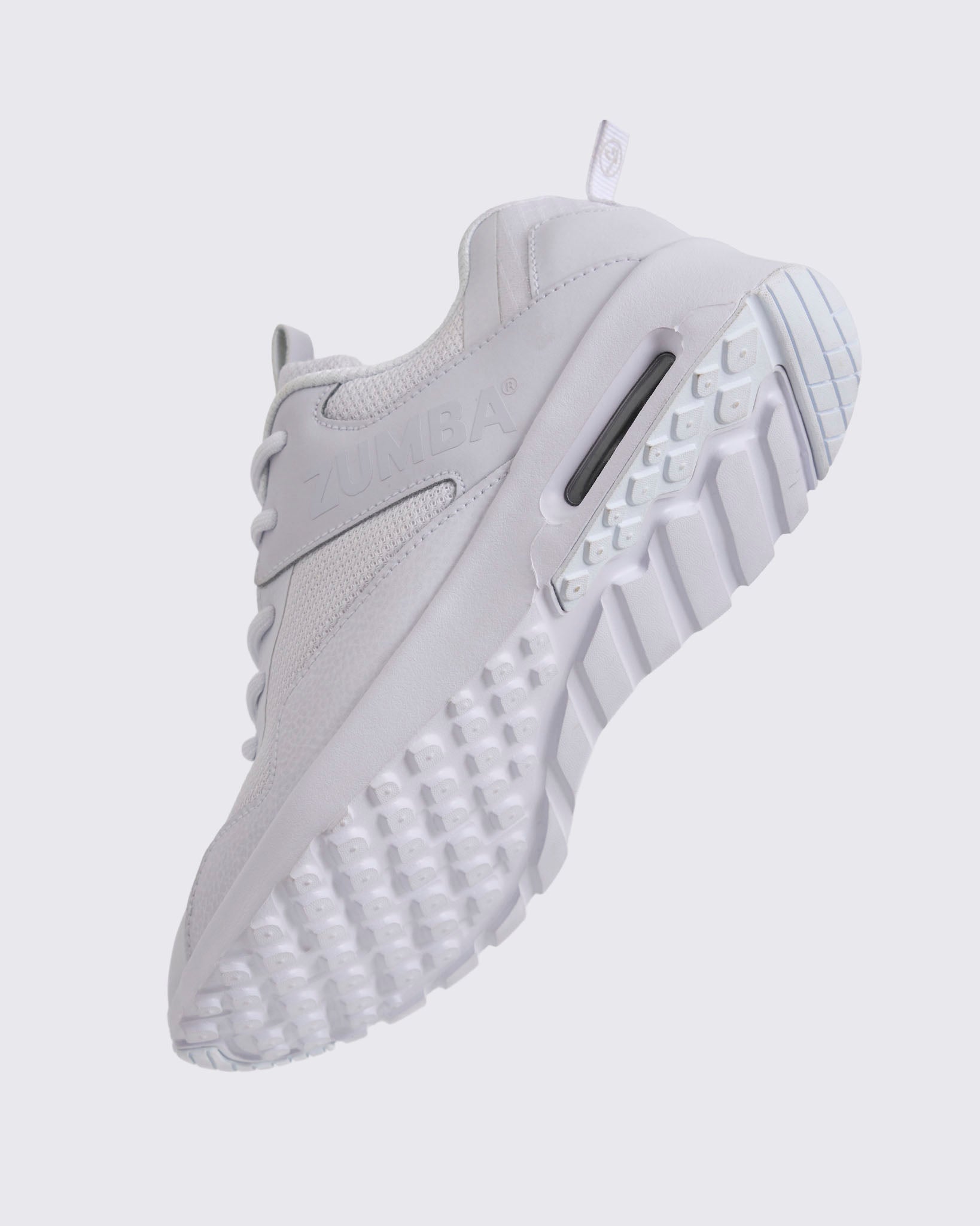White Zumba low-top athletic sneaker shown from the bottom angle, emphasizing the textured lug outsole, deep grooves, and visible air cushioning in the heel.