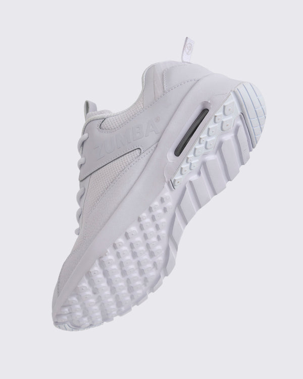 White Zumba low-top athletic sneaker shown from the bottom angle, emphasizing the textured lug outsole, deep grooves, and visible air cushioning in the heel.