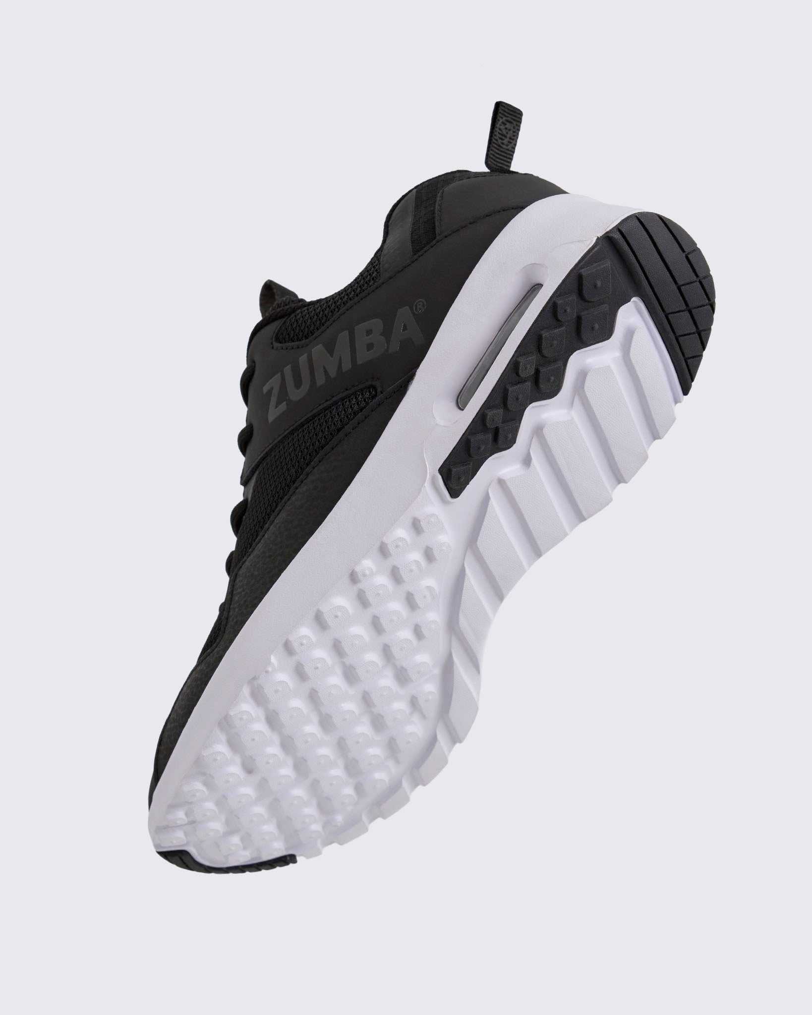 Black Zumba low-top athletic sneaker shown from the bottom angle, emphasizing the textured lug outsole, deep grooves, and visible air cushioning in the heel.