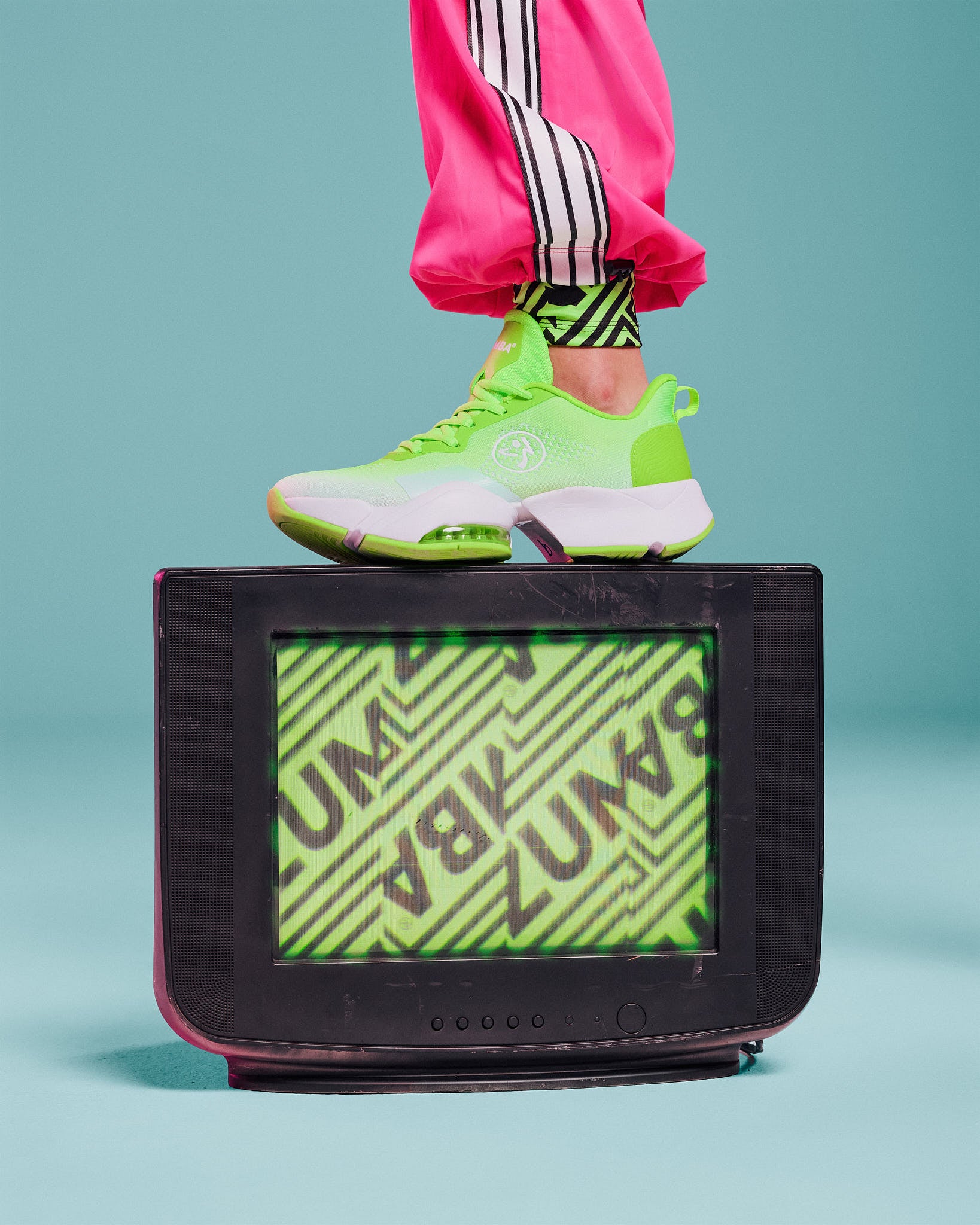Neon green high-top sneaker with a white sole and Zumbito logo, propped on a vintage TV against an aqua background.