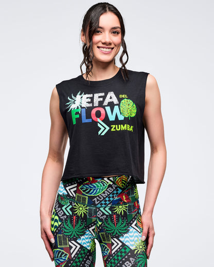 Black cropped sleeveless muscle tank with “JEFA DEL FLOW ZUMBA” multicolor graphic on the chest, modeled by a female wearing colorful tropical-print leggings on a white studio background.