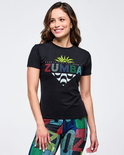 Front close-up of a black crewneck “ZUMBA” graphic tee with multicolor lettering and palm graphic, worn with high-waisted, multicolor letter-print leggings on a smiling female model against a white backdrop.