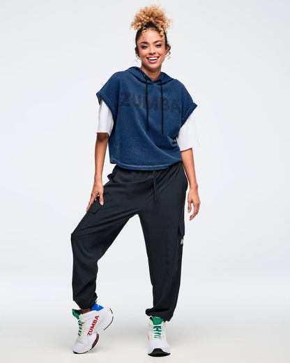 Full-body view of a navy denim short-sleeve hooded sweatshirt layered over a white tee, styled with black cargo jogger pants and white high-top sneakers with green accents on a female model against a white background.