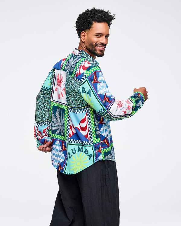 Multicolor patchwork Zumba button-up shirt featuring tropical and wave-print panels with checkerboard borders. Male model wears the long-sleeve collared shirt with wide-leg black pants on a light gray studio background.