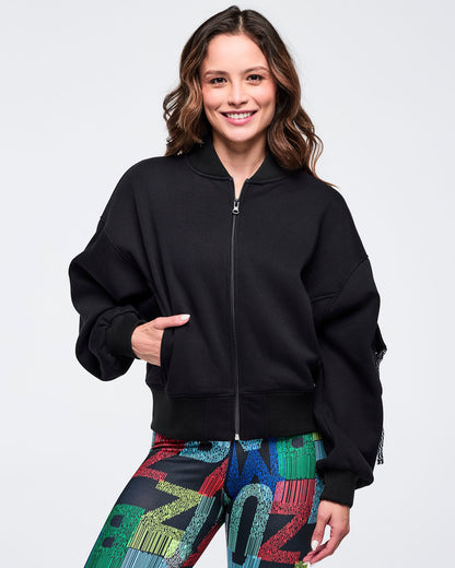 Front view of a black zip-up jacket with ribbed collar, cuffs, and hem; female model pairs it with multicolor letter-print leggings on a white background.