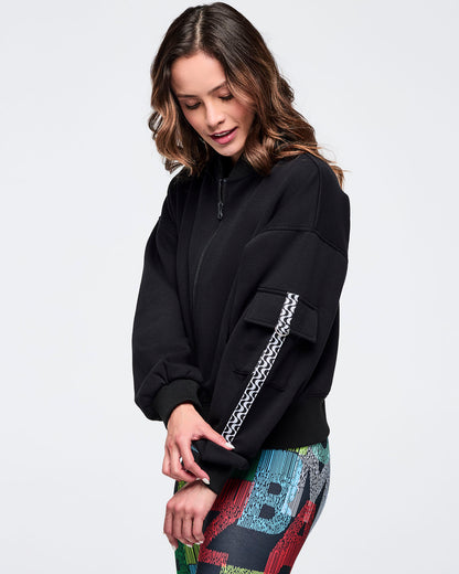 Black zip-up jacket featuring a sleeve cargo pocket and black-and-white wavy trim detail; female model wears multicolor letter-print leggings on a white background.