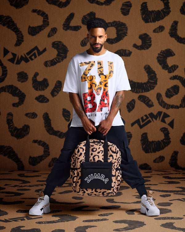 Leopard print backpack held by a male model in a white graphic tee, black cargo joggers, and white high-top sneakers against  leopard print backdrop.