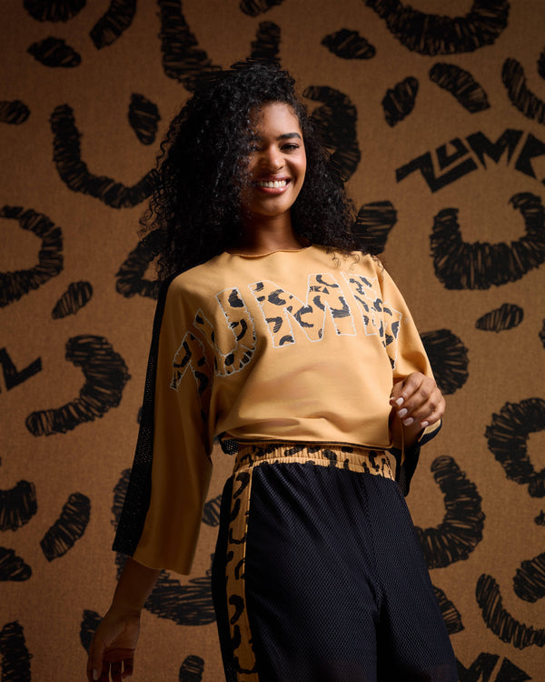 Tan Zumba sweatshirt on female model with black mesh cheetah stripe pants against a tan cheetah print backdrop.
