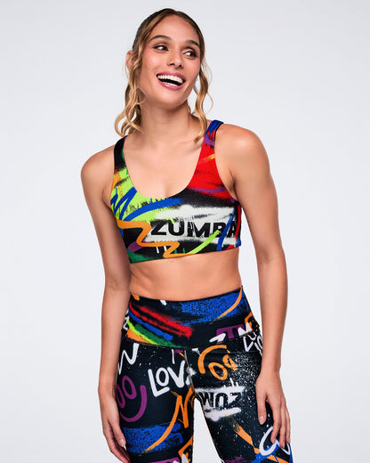 Female model wearing a colorful Zumba sports bra and leggings on a white background.