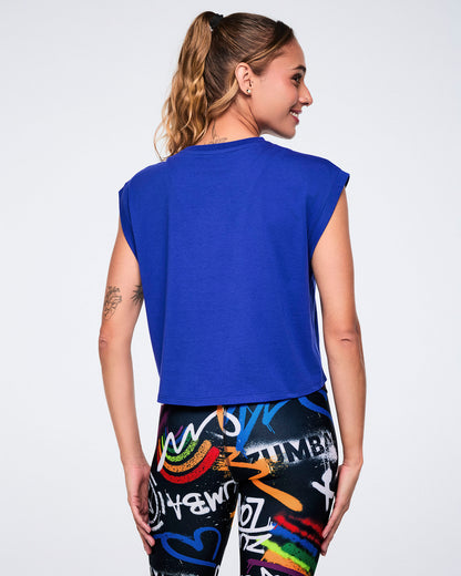 Female model wearing a blue sleeveless top, shown from the back, paired with colorful leggings on a white background.