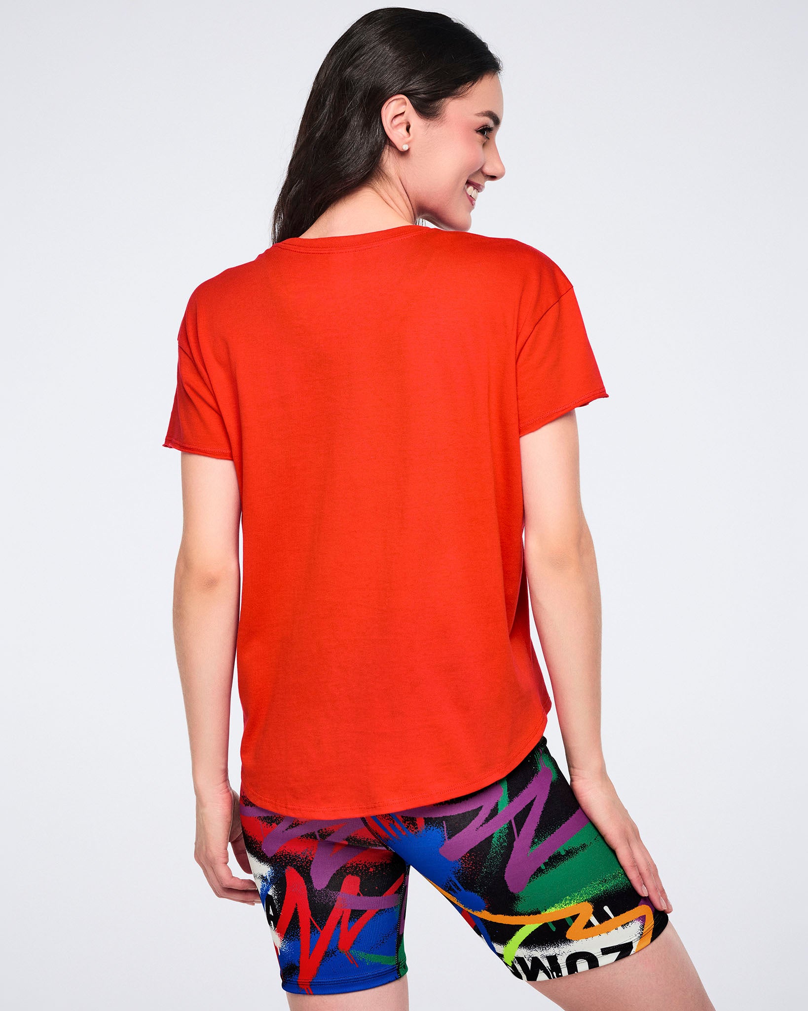 Female model, shown from the back, wearing a red shirt and colorful biker shorts on a white background.