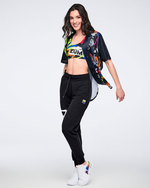 Female model in colorful Zumba crop top, black joggers, and white sneakers posing against a white background.