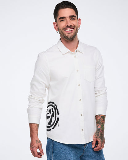 Male model wearing a white button-down shirt with a black 'Zumbito' and wearing it with denim cargo pants, against a white background.