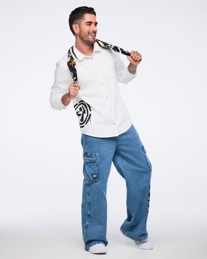 Male model holding a colorful bandana behind his neck, while wearing a white button-down shirt and denim cargo pants against a background.