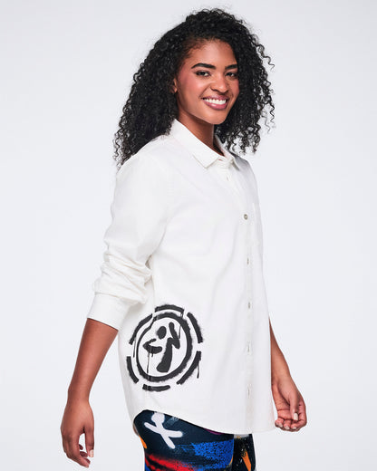 Female model wearing a white button down with a black 'Zumbito' on a white background.