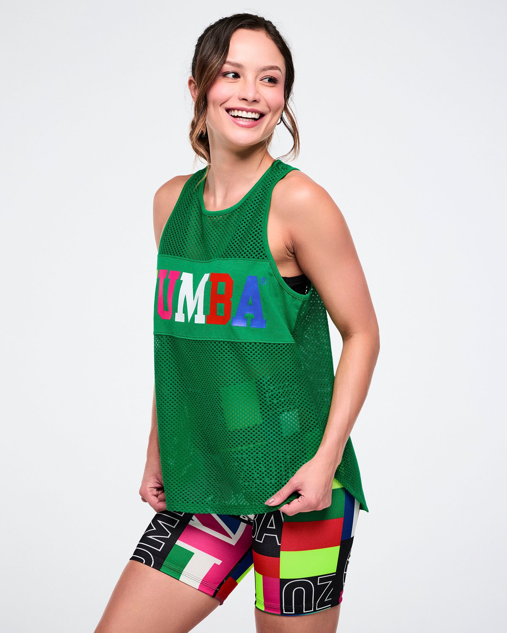 Female model wearing a green tank top with 'Zumba' text and colorful shorts on a white background.