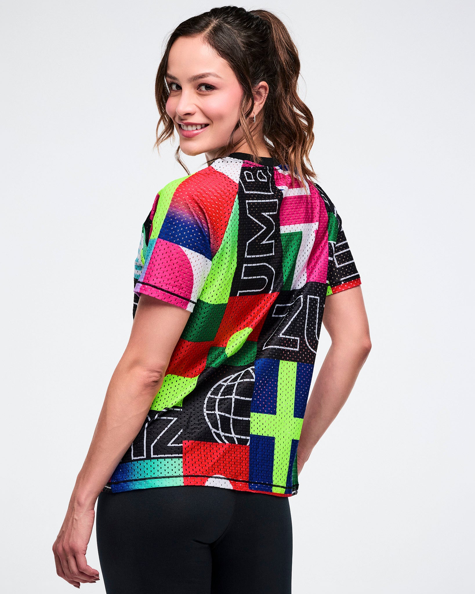Back view of a female model wearing a colorful mesh crew neck top against a white background.