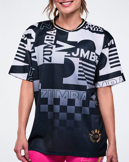 Close up of a female model wearing a black and white Zumba shirt with various patterns on a white background.