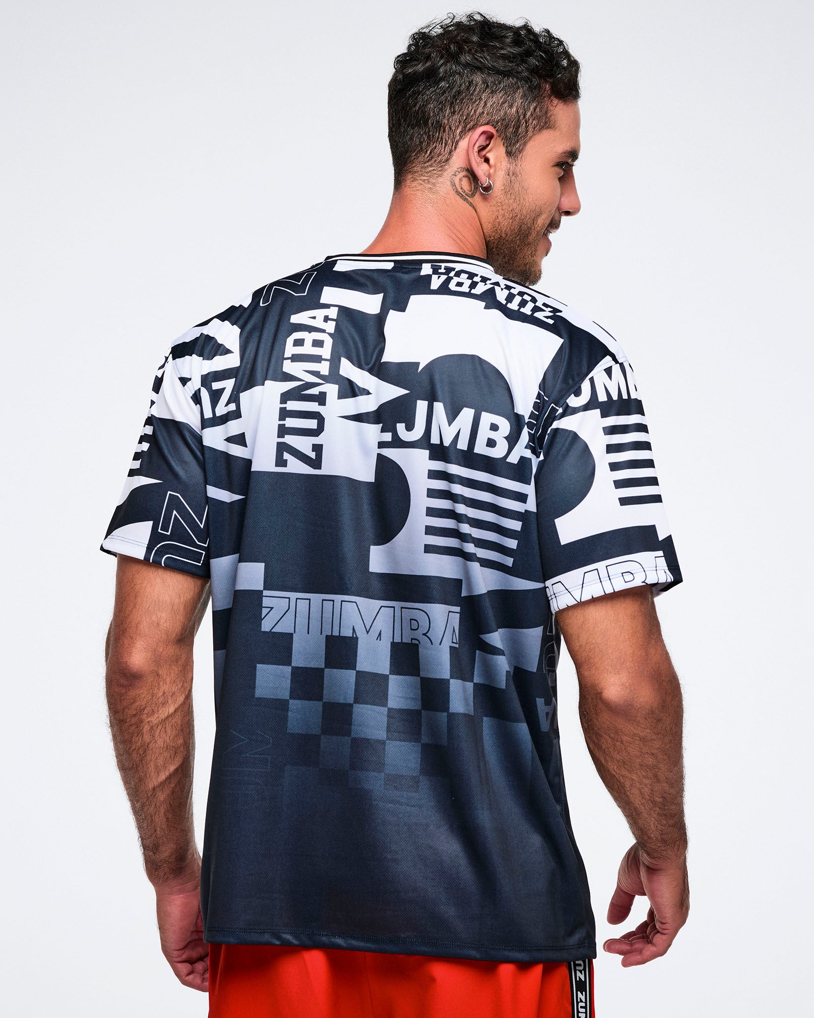 Back view of a male model wearing a black and white patterned Zumba shirt on a plain background.