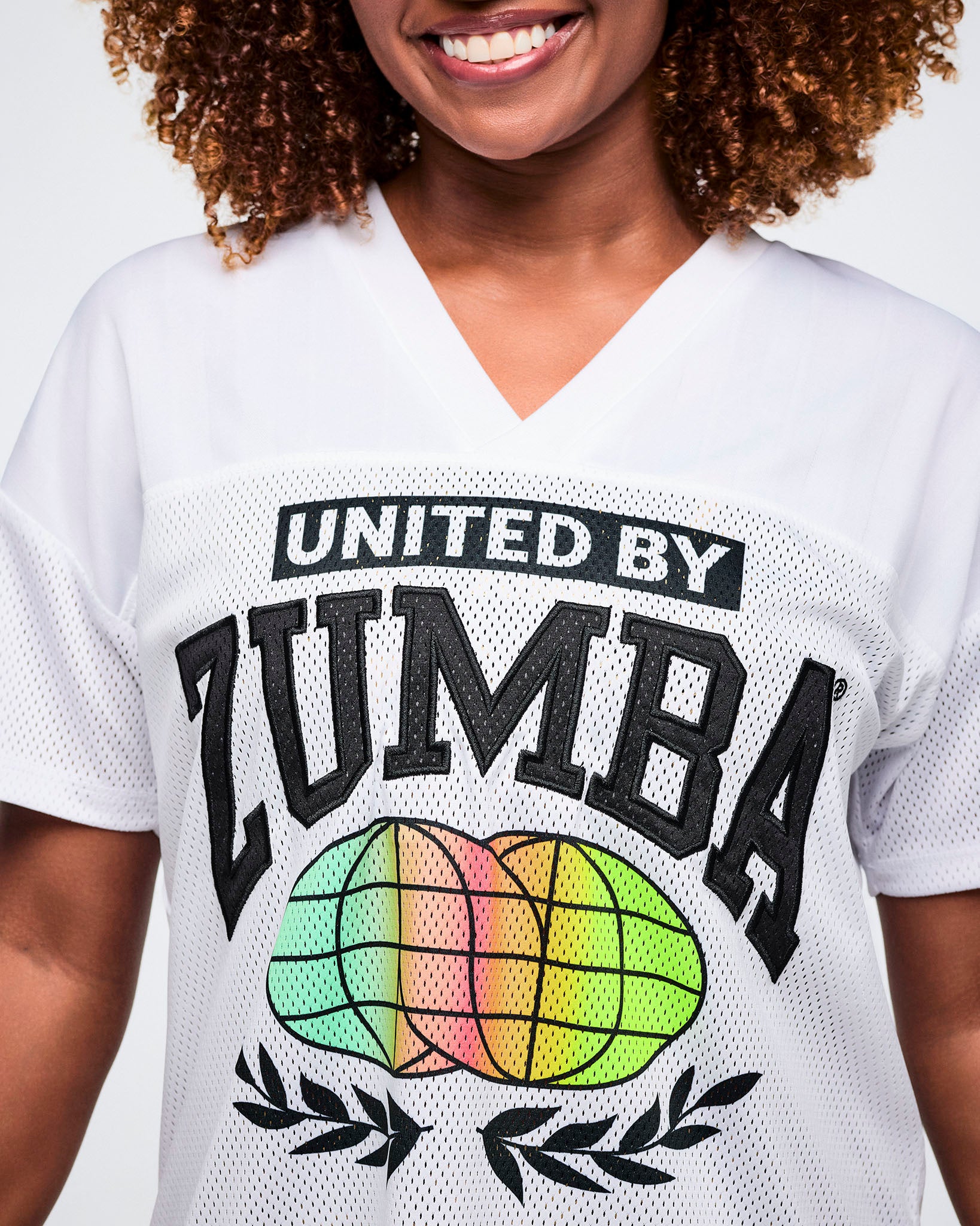 Close up of a female model wearing a white 'United by Zumba' top with a colorful globe design.
