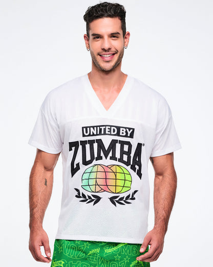 Male model wearing a white 'United by Zumba' top with colorful graphics on a white background.