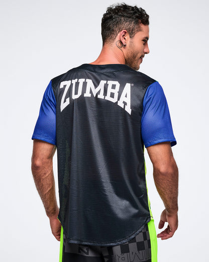 Back view of a male model wearing a black Zumba shirt with blue sleeves with Zumba in white text, on a plain background.