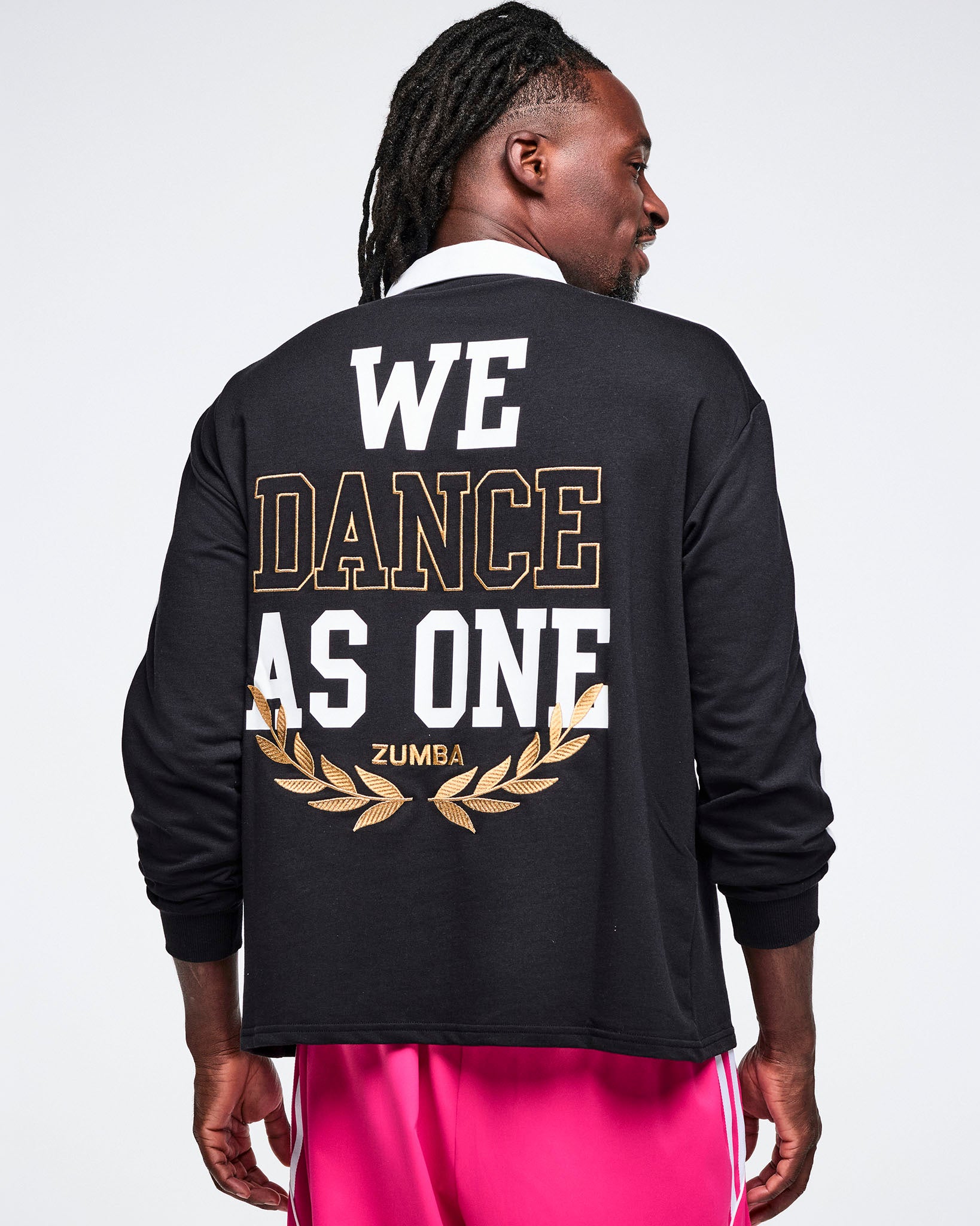 Male model wearing a black Zumba polo with 'We Dance As One' Zumba text on the back.