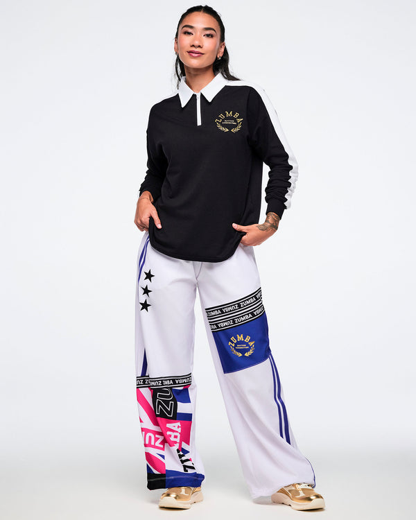 Female model wearing a black and white polo with colorful white pants on a white background.