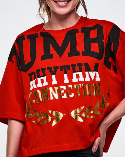 Close-up of a female model wearing a red 'Zumba Rhythm Connection' top with gold accents on a white background.