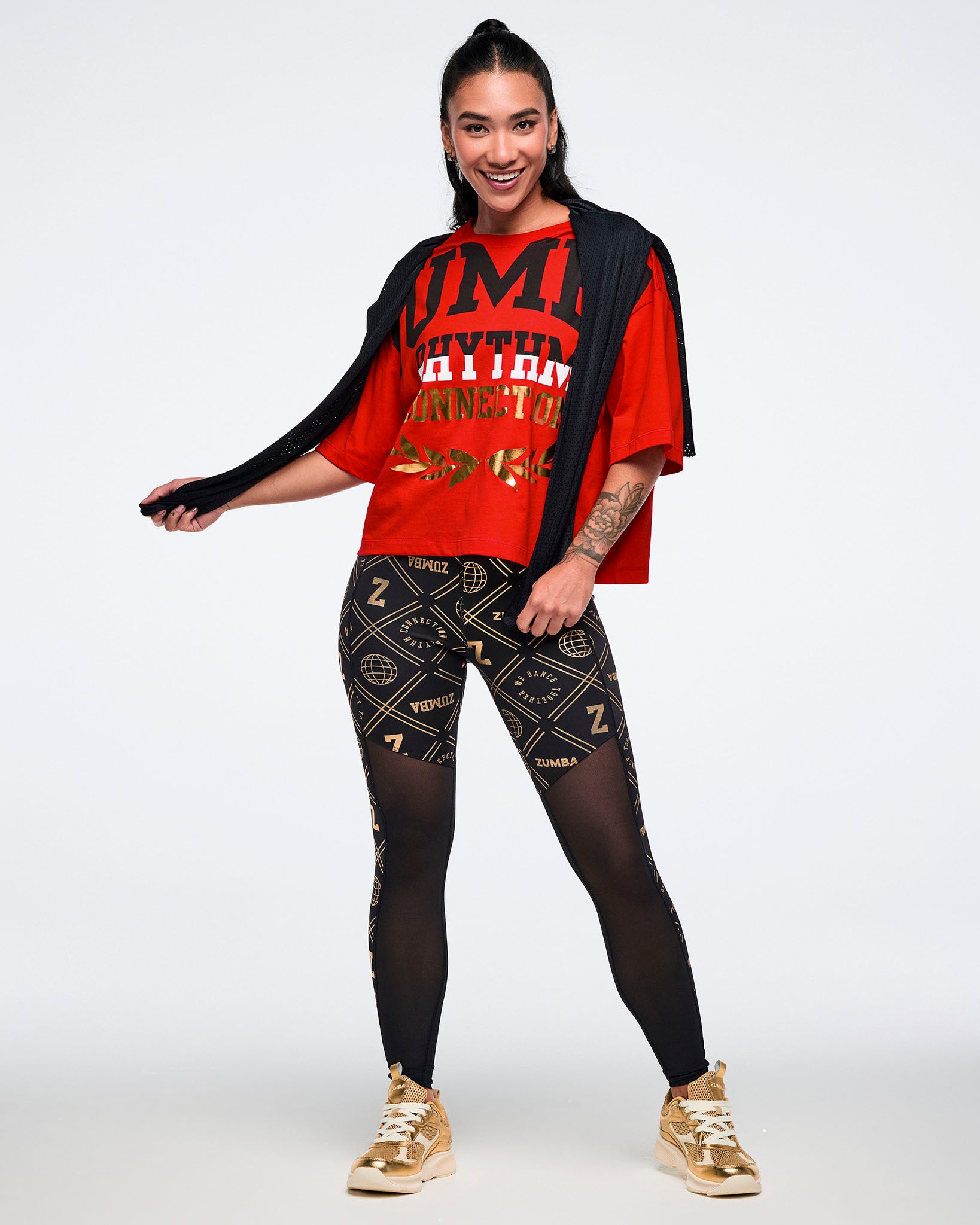 Female model wearing a red oversized t-shirt with text and black and gold patterned leggings on a white background.