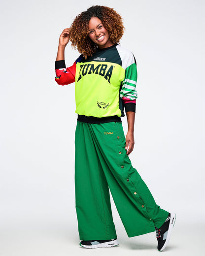 Female model in a colorful Zumba top paired with green snap pants, set against a white background.