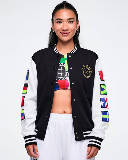 Female model wearing a colorful varsity jacket unbuttoned with a multi color bra top showing all against a white background.