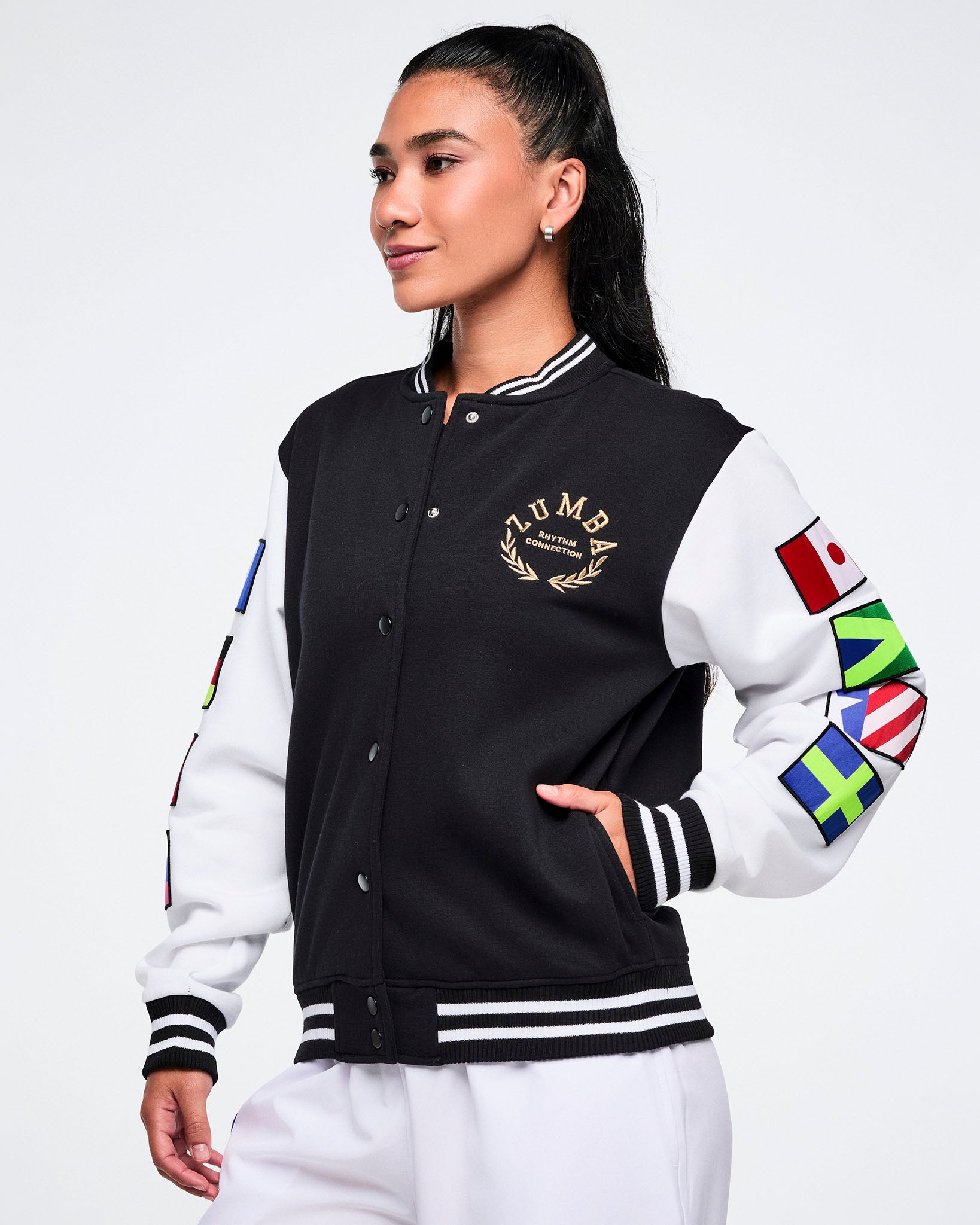 Female model wearing a black and white varsity jacket with international flag designs on sleeves against a white background.