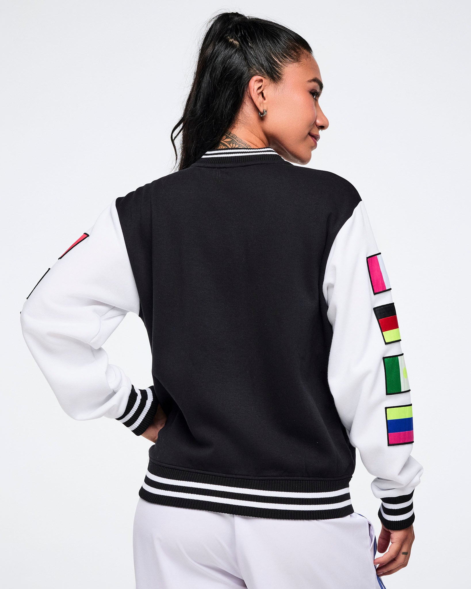 Female model with the back view of a black and white varsity jacket with colorful flag sleeves on a white background.