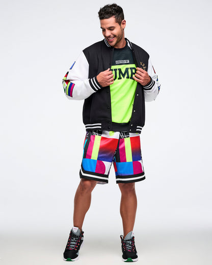 Male model wearing a colorful Zumba t-shirt with an unbuttoned varsity jacket and multi-colored shorts on a white background.