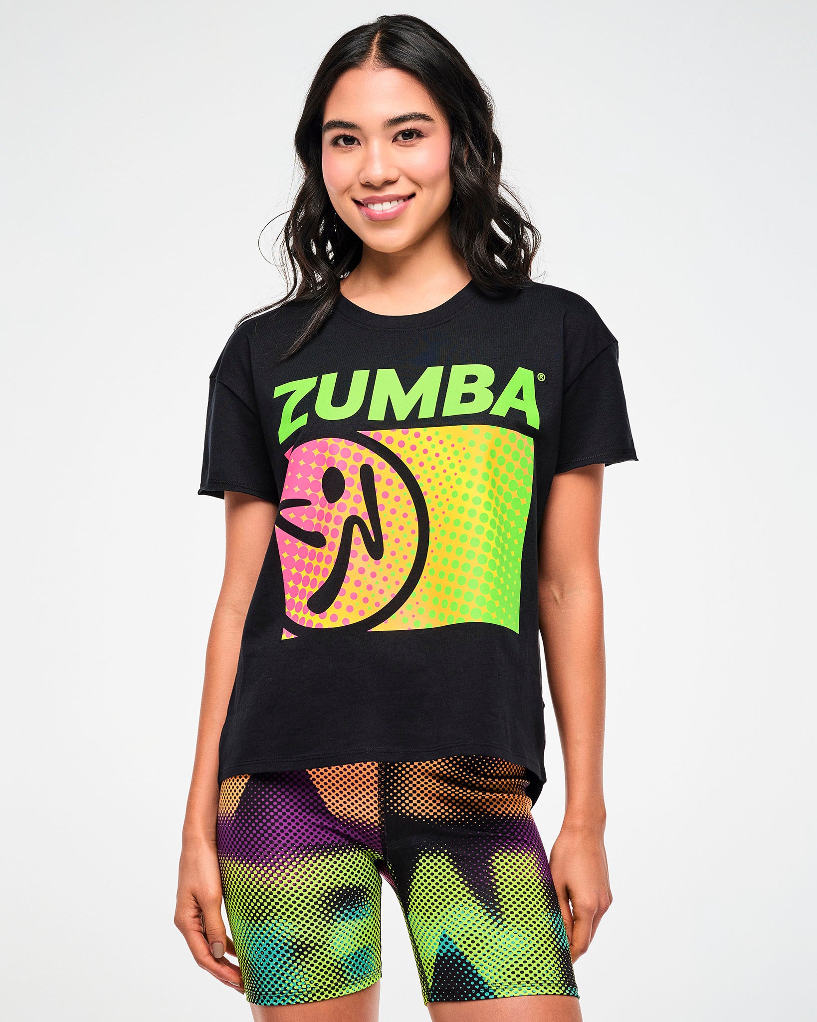 Female model wearing a black tee with a dot pattern "ZUMBA" logo graphic, paired with matching dot pattern biker shorts.