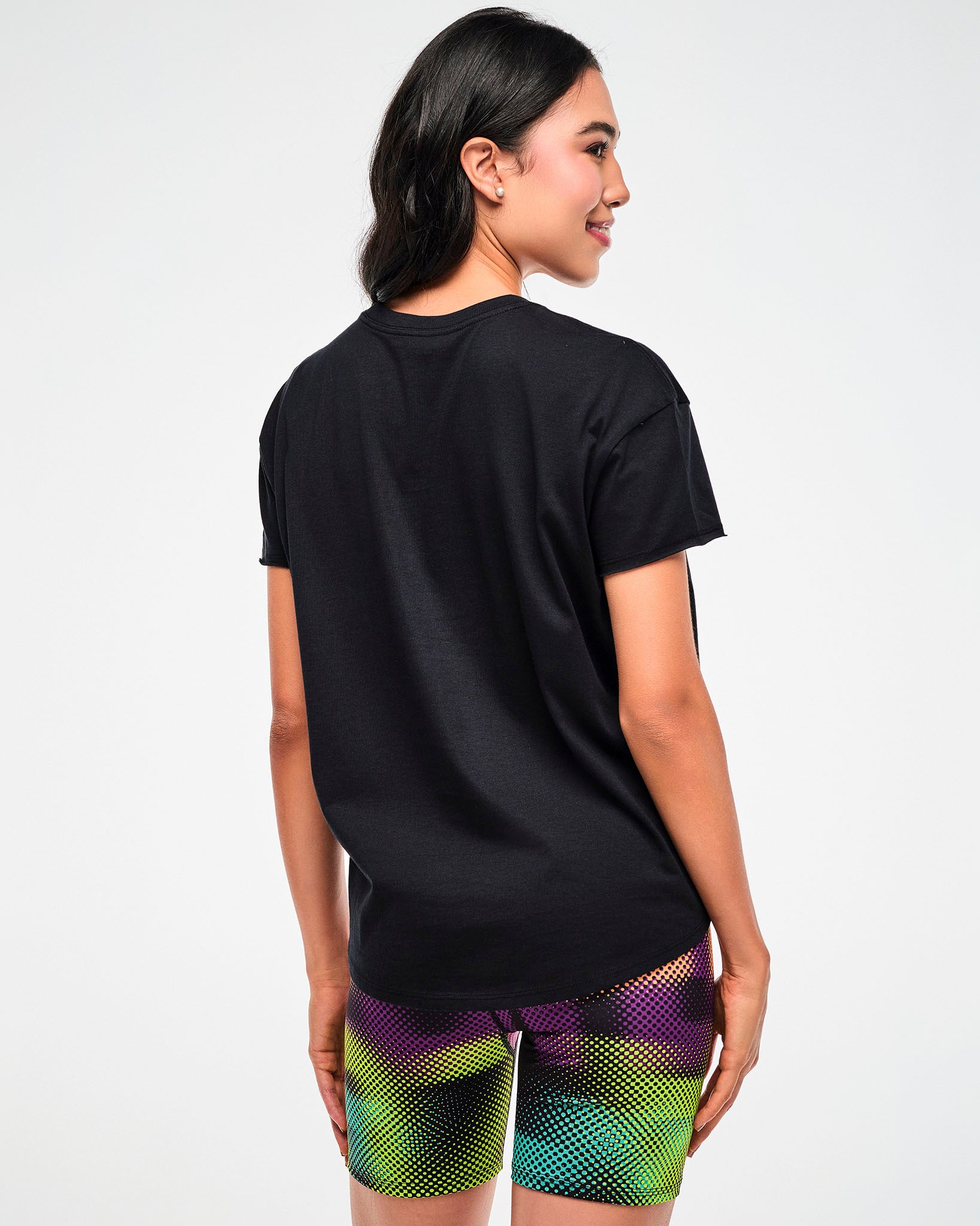 Shown from the back, female model wearing a black tee, paired with purple, green, and yellow dot pattern biker shorts.