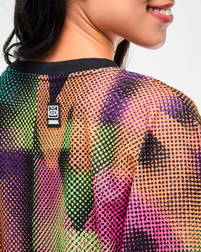 Close-up of the mesh fabric and a black tag featuring a cassette tape icon and "ZUMBA" text, both in white, on the back of a crop top with a blurred wordmark print.